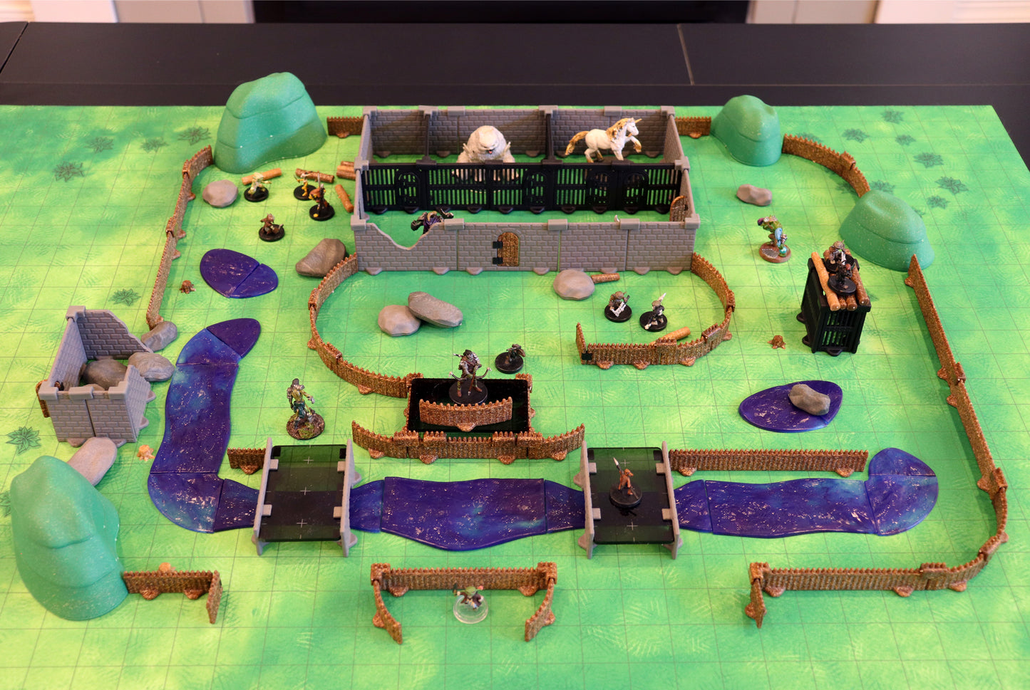 Wide-scale shot of the Bandit Camp Adventure Set laid out on a large battlemat, showing the full perimeter of palisade fencing and the scattered terrain elements for an epic encounter.