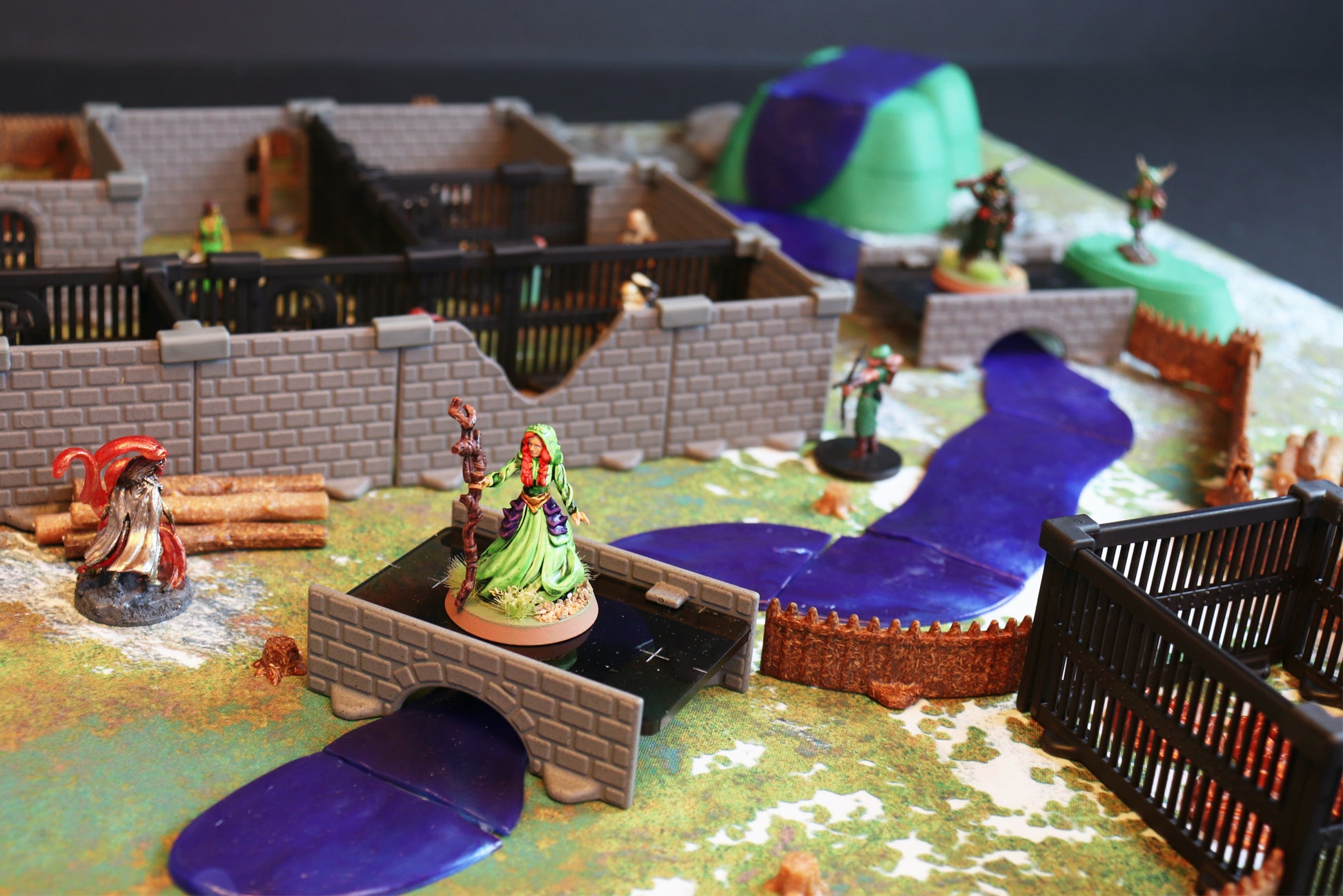 Detailed scene showcasing the integration of modular terrain sections (hills/river pieces) and a bridge with the structural walls of the Bandit Camp Set, setting a scene for a wilderness encounter.