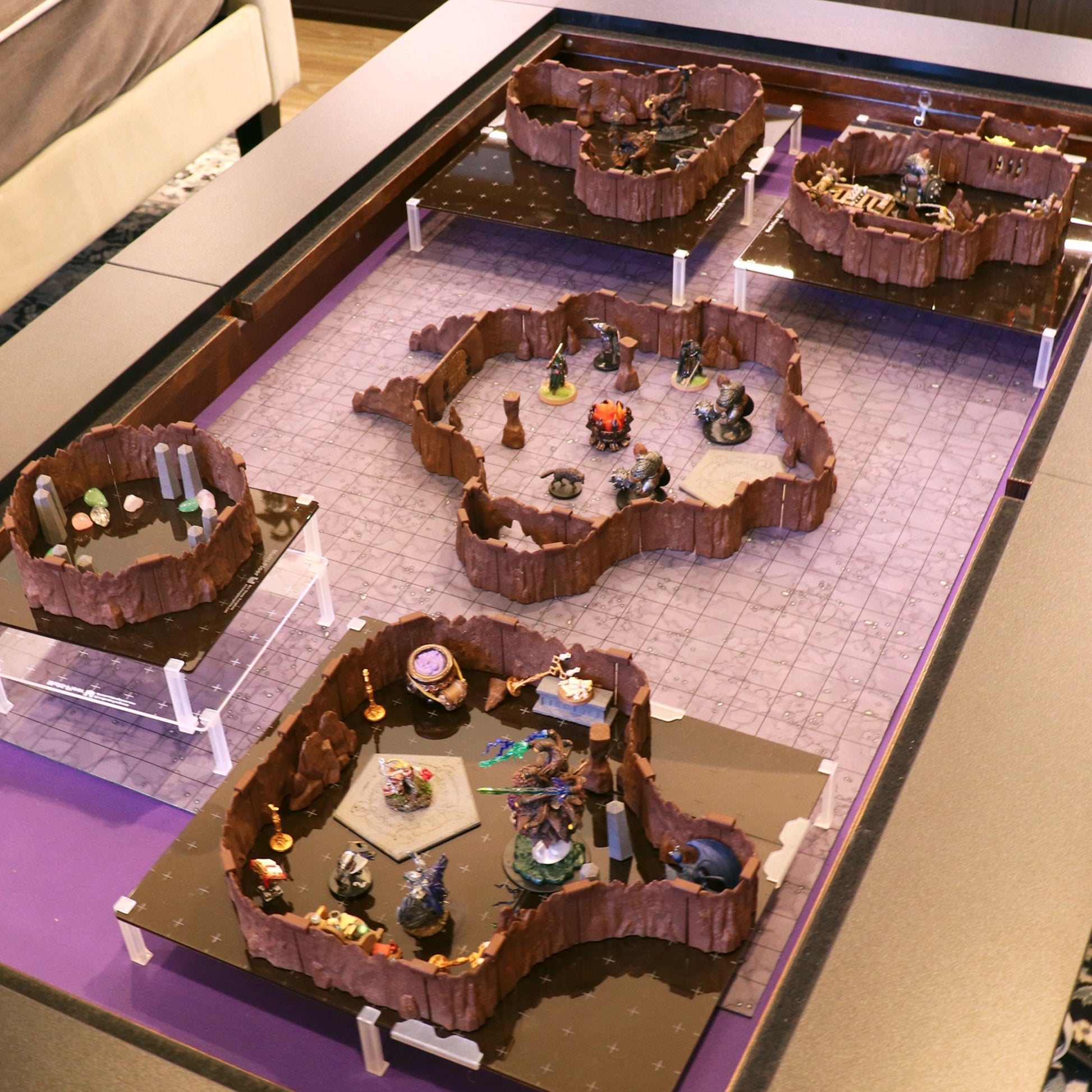 High-angle shot of a multi-tier cavern dungeon setup using acrylic risers to create elevated platforms with the modular Troll Cavern terrain. The scene features miniatures and scatter pieces on a grid mat.