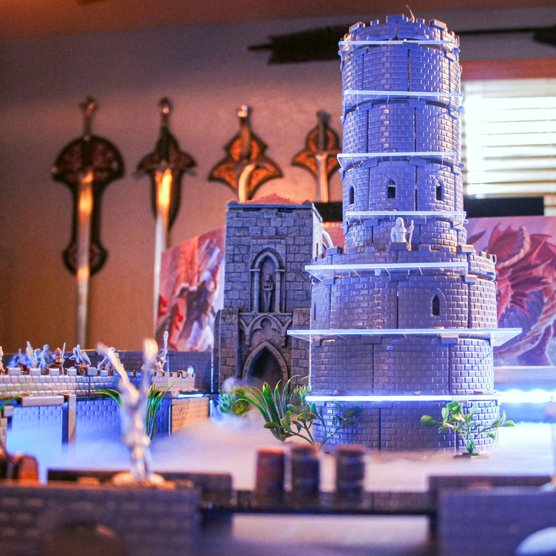 Atmospheric scene of the modular Wizard's Tower build with miniatures, illuminated by a dramatic blue light source. The rounded castle walls and windowed walls are clearly visible.