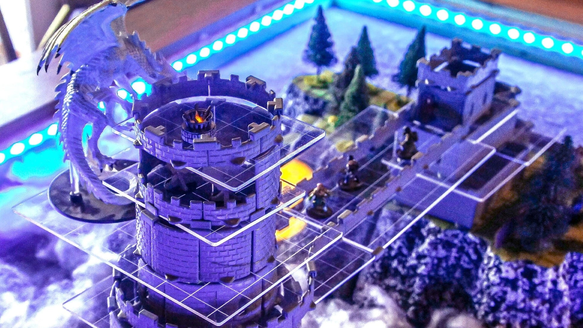 High-angle view of a multi-story Wizard's Tower Set build, showing the internal structure with acrylic platforms for different levels, populated by miniatures and a large dragon on the roof.