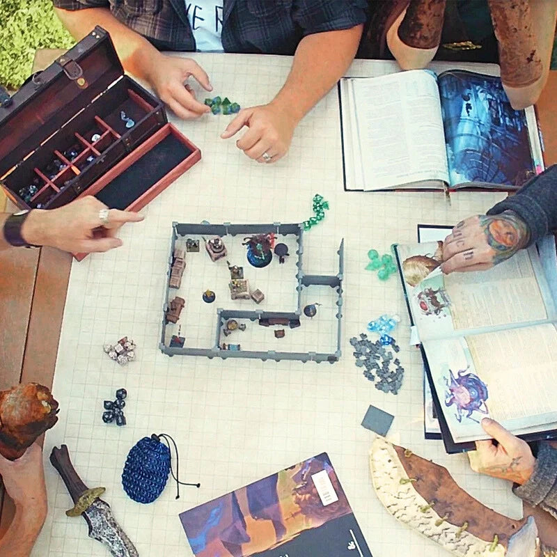 A top-down view of a table where people are playing Dungeons and Dragons using various dice, books, and a Mini Ruins Kit.
