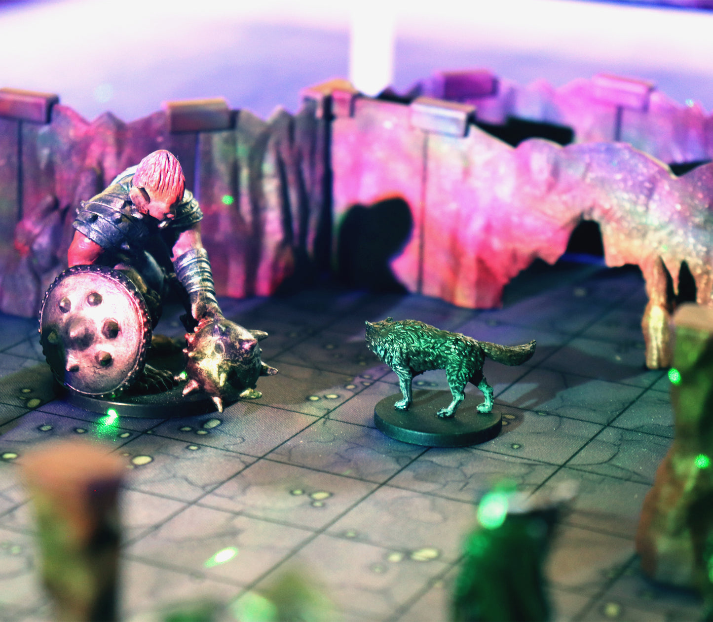 Close-up of a tabletop RPG battle featuring a giant miniature and a wolf miniature inside cavern terrain walls with colorful lighting effects.