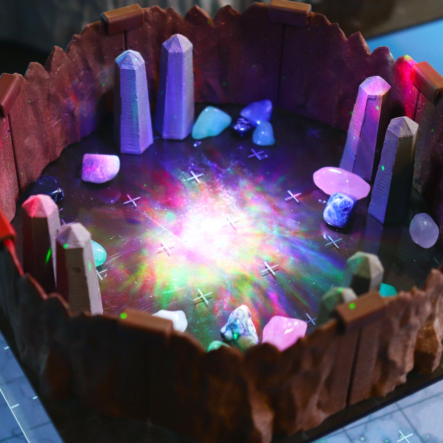 Close-up of Obelisk scatter terrain pieces and colored gemstones inside modular cavern walls, illuminated by a brilliant, multi-colored light effect.