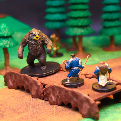 TTRPG scene featuring miniatures of an armored warrior and a large bear creature battling on a modular Rock Bridge piece in a forest setting.