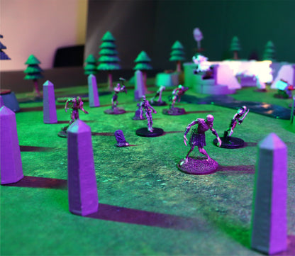 Low-angle shot of purple-lit Obelisks and a gravestone creating a cemetery terrain scene, with a horde of zombie miniatures advancing across the grass mat.
