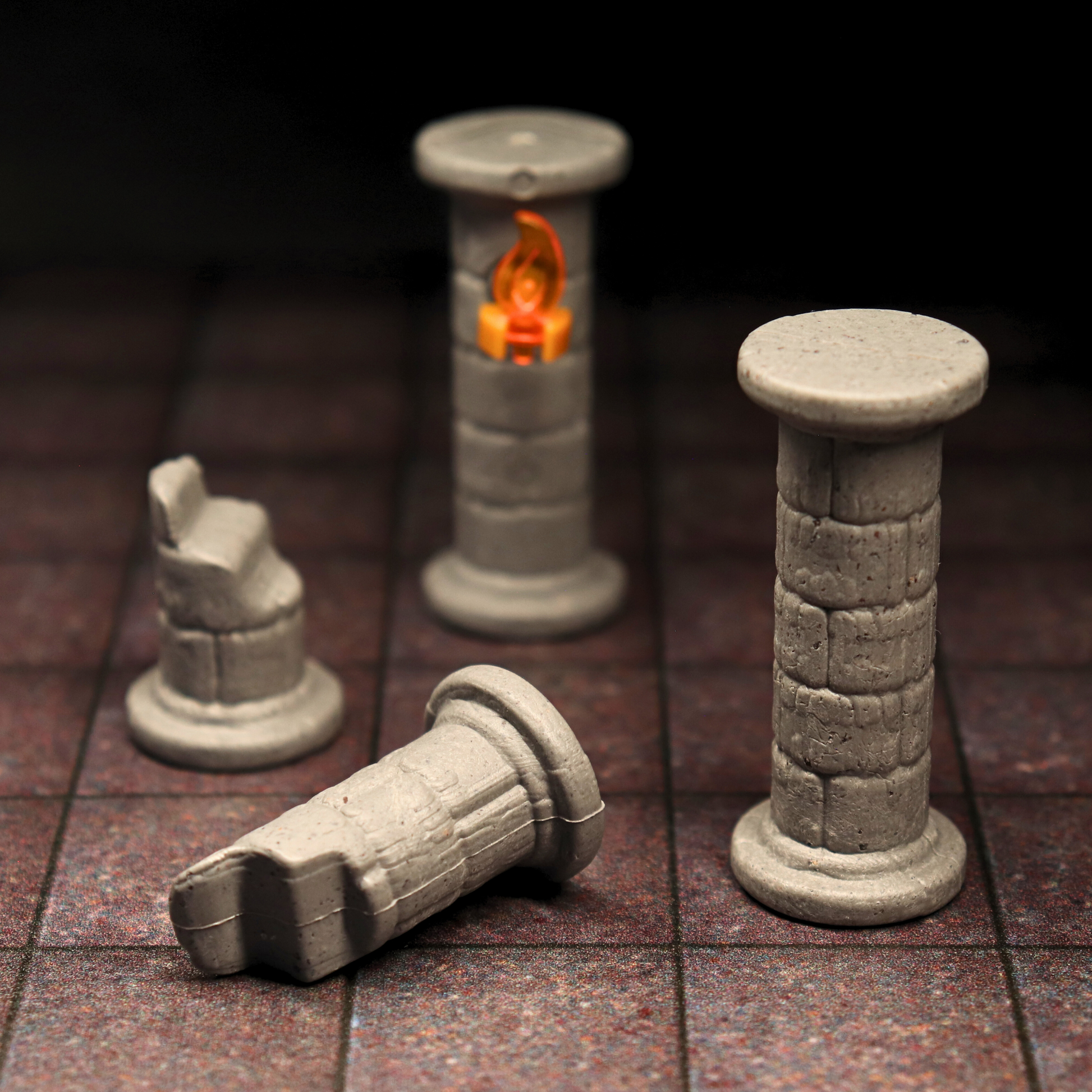 Close-up of broken and full stone pillars with an attached, glowing torch flame on a square-gridded dungeon map tile.