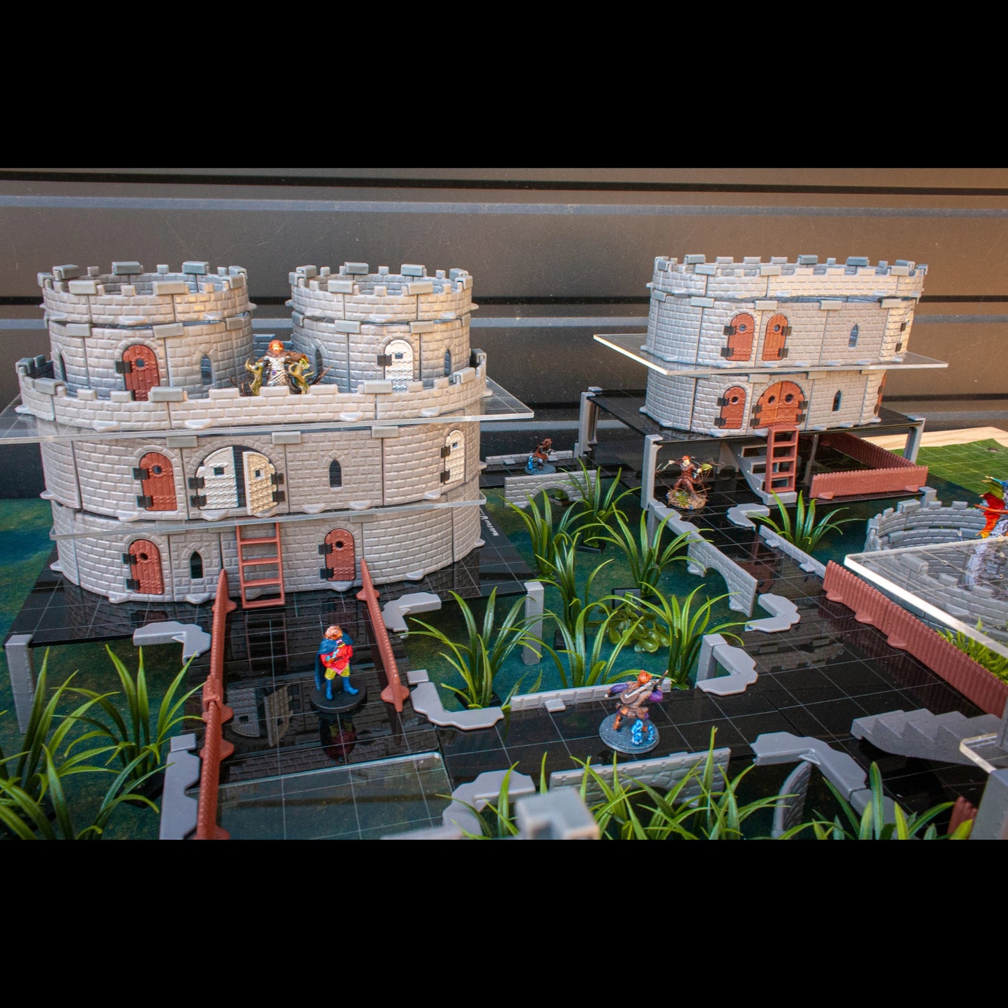 Dark gray acrylic platforms blending with textured cliff terrain to create a multi-level vertical drop in a dungeon encounter.