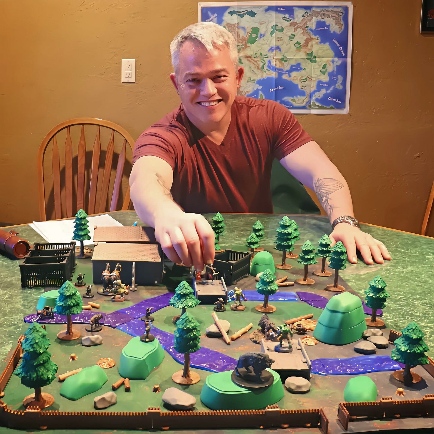 A smiling Dungeon Master placing a miniature on a large, custom forest terrain layout built using the Dark Pine Forest Kit.