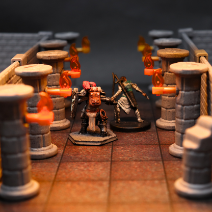 Dungeon terrain setup with stone pillars and bright torches, featuring two tabletop miniatures exploring in a narrow corridor.