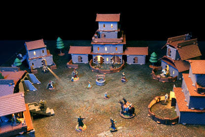 Epic fantasy village battle scene at night on a cobblestone map, featuring multi-story 3D buildings with brown Village Roof Kit tiles.