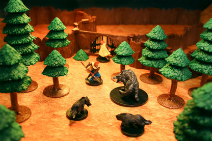 Forest encounter scene showing a hero miniature fighting multiple bear miniatures among dense pine trees near a cavern wall with gate.