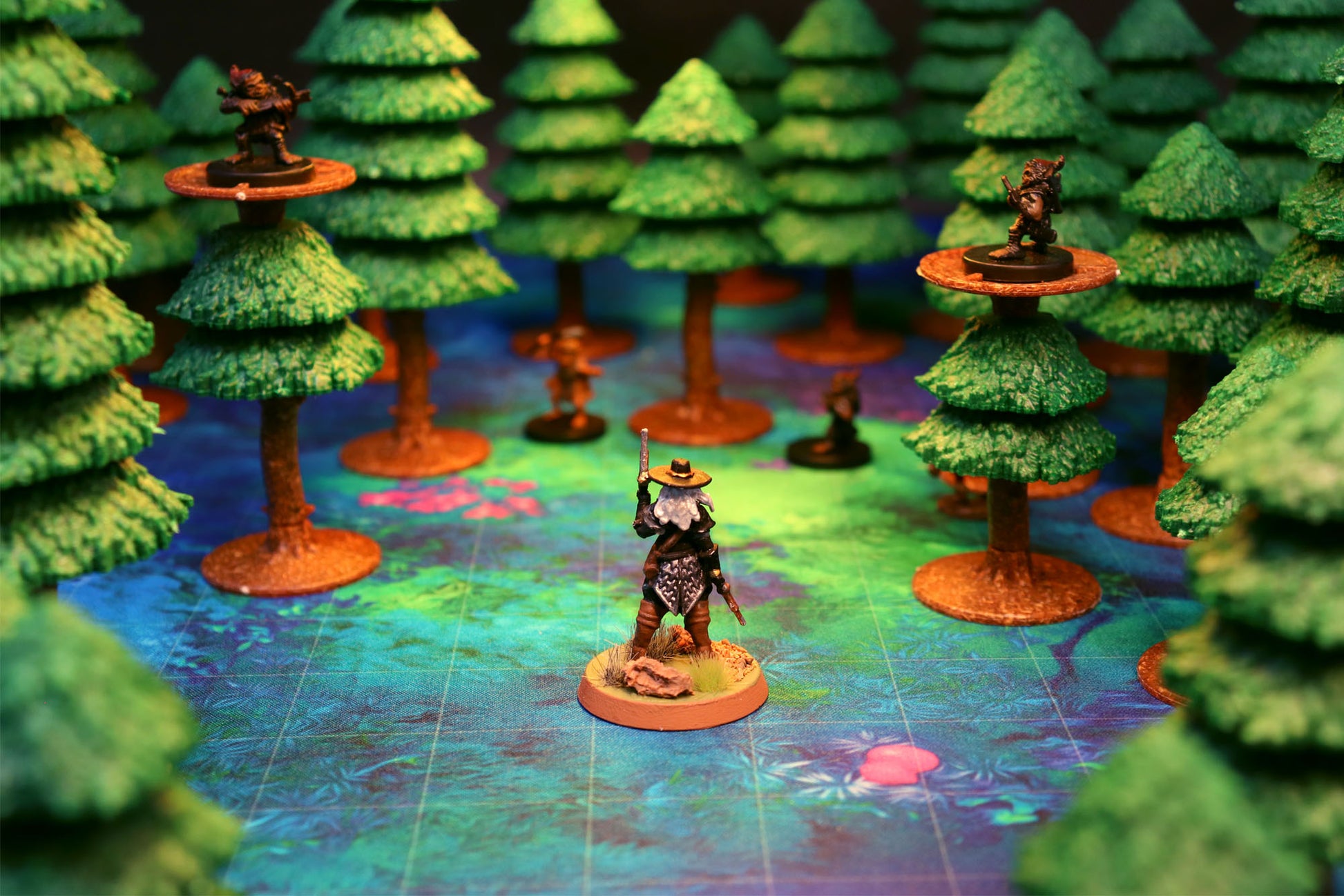 A ranger miniature standing in a dark forest with two other miniatures placed on high-ground tree platforms using the modular trees.