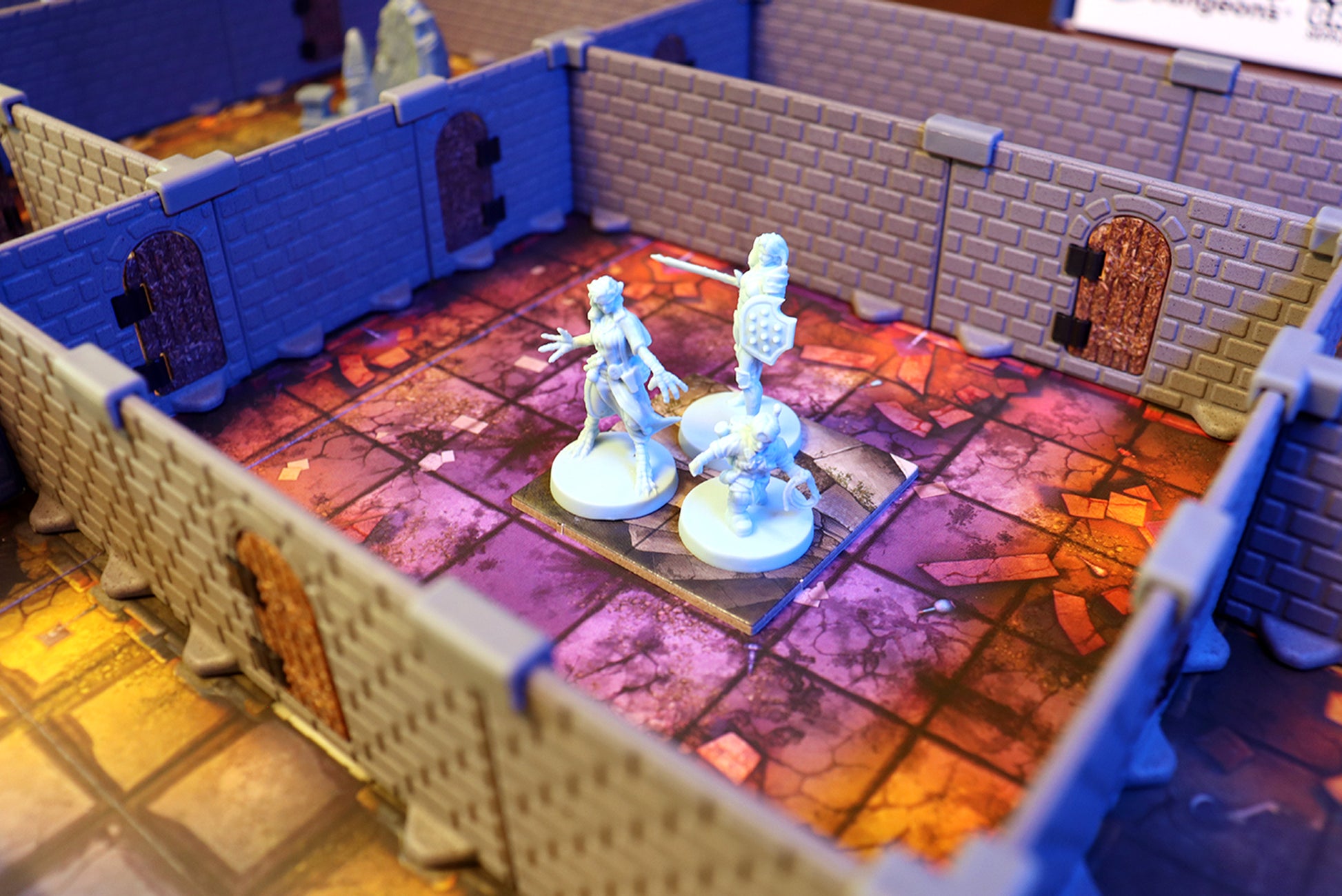 Two hero miniatures fighting in a dungeon room built with the AQ Set, showcasing the low-profile walls and the dramatic purple map tile.