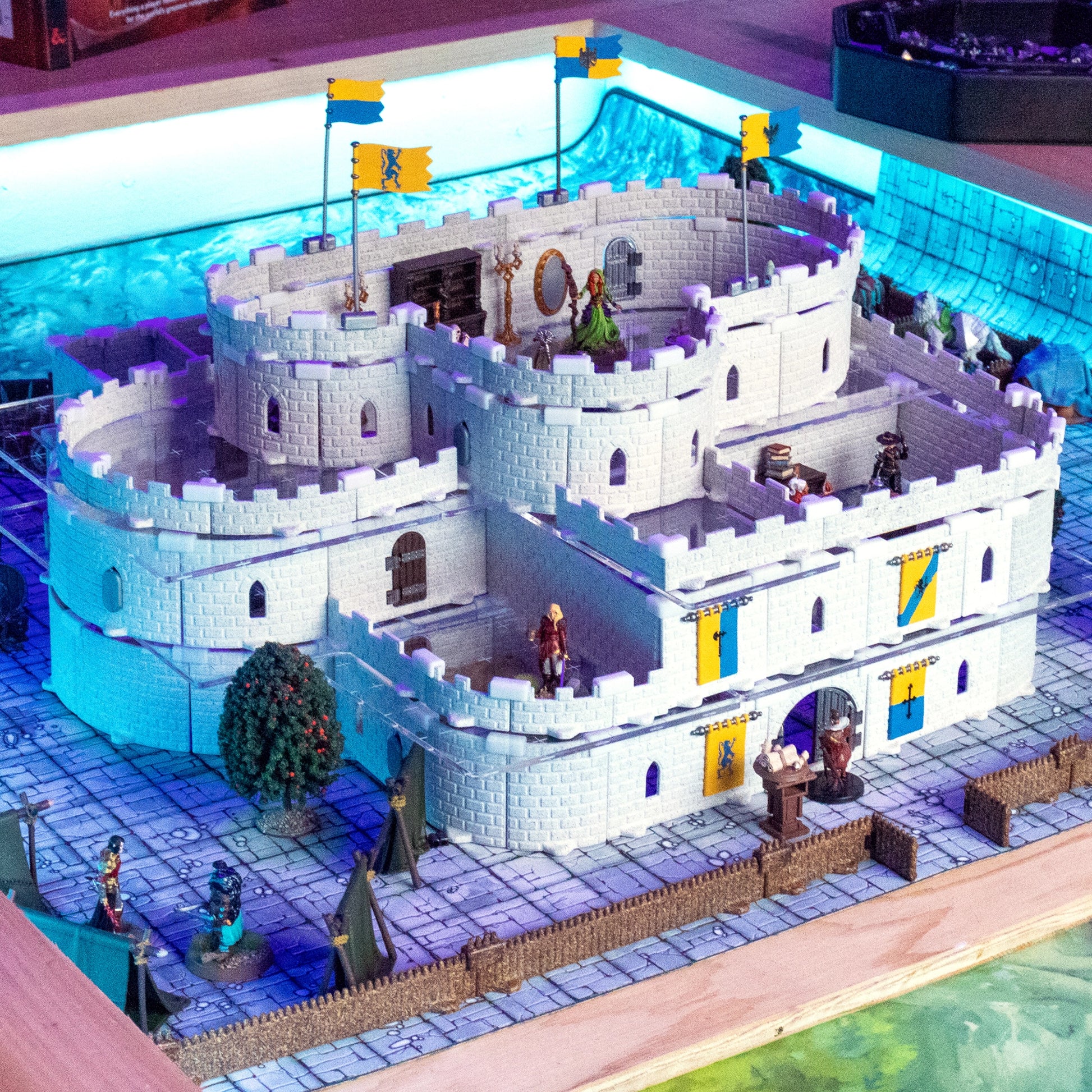 An impressive, sprawling Regent Castle Core Set build featuring multi-story white modular castle walls, rounded towers, and banners. The setup includes various miniatures in a vibrant D&D fantasy setting, showcasing its versatile modular design.