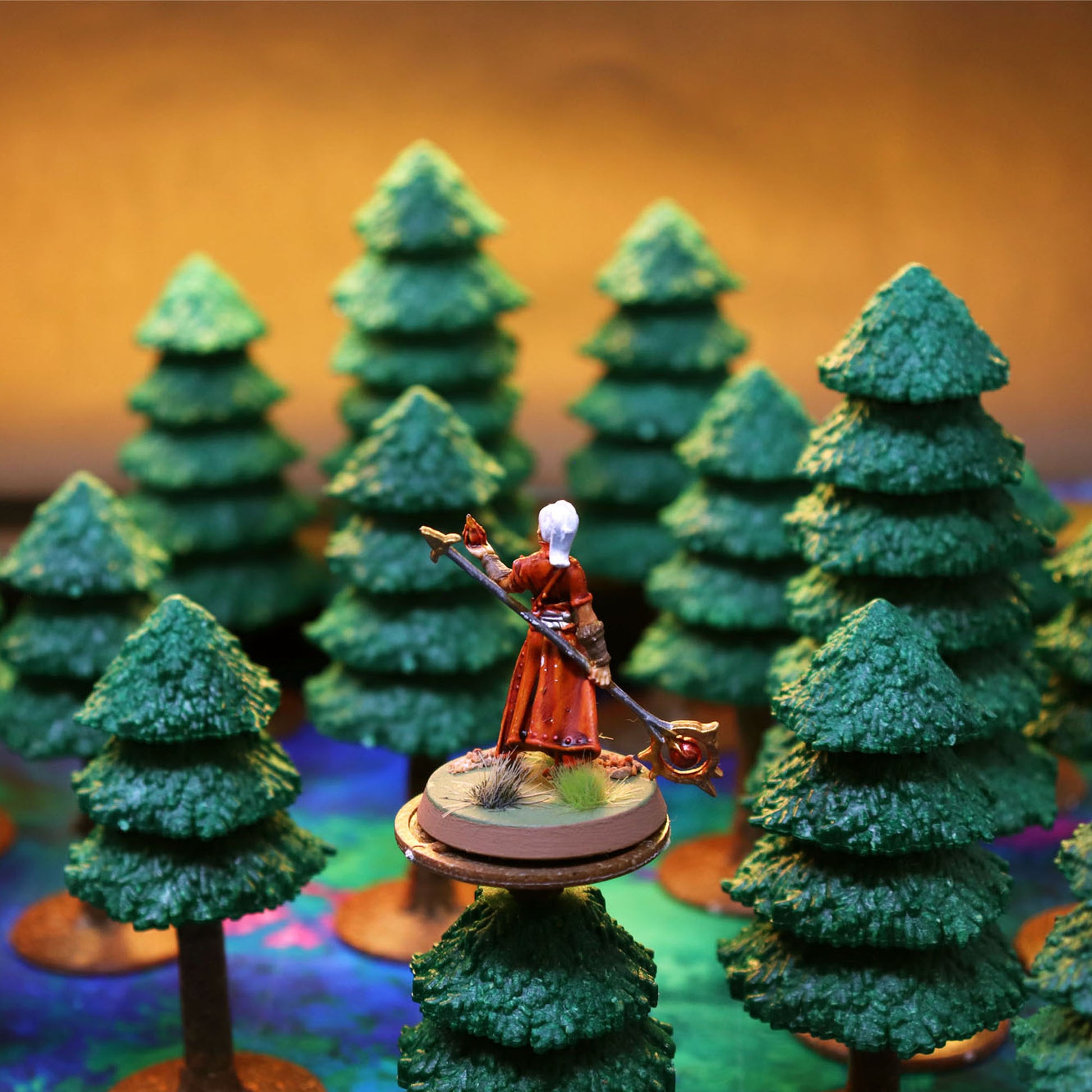 Close-up of a wizard miniature standing in a dense pine forest terrain setup, demonstrating line-of-sight obstruction.